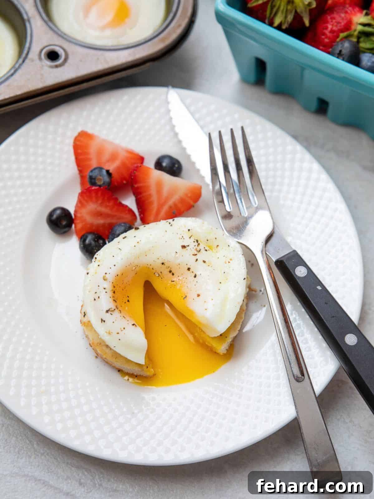 Oven Poached Eggs Recipe Oven Poached Egg on English muffin cut open with yolk running out onto plate, showcasing its perfect runniness.