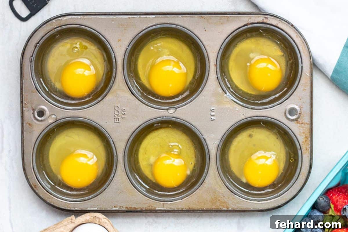 Poaching Eggs in Oven Prep A muffin tin neatly filled with 6 cracked eggs, one perfectly placed in each cup, ready for oven poaching.