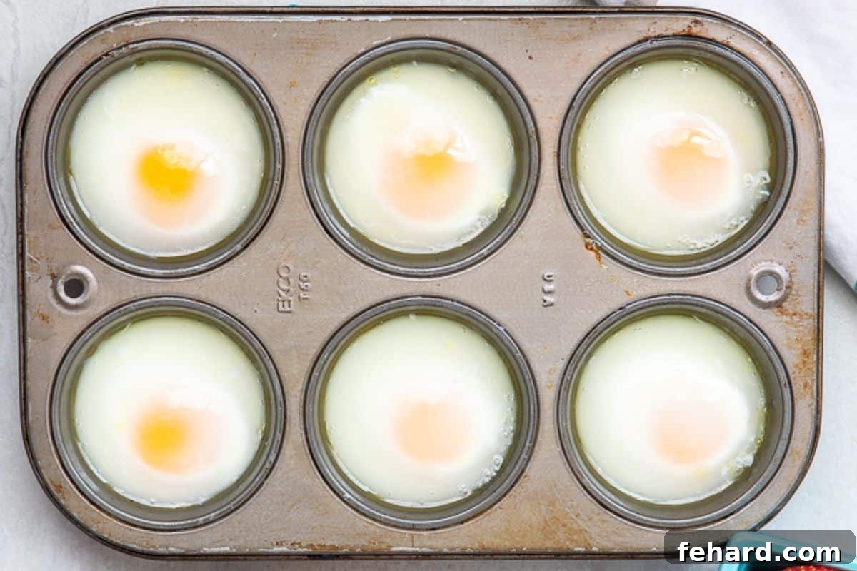 Muffin Tin Poached Eggs Cooked A muffin tin showcasing 6 perfectly oven-poached eggs, each one ready to be removed and served.