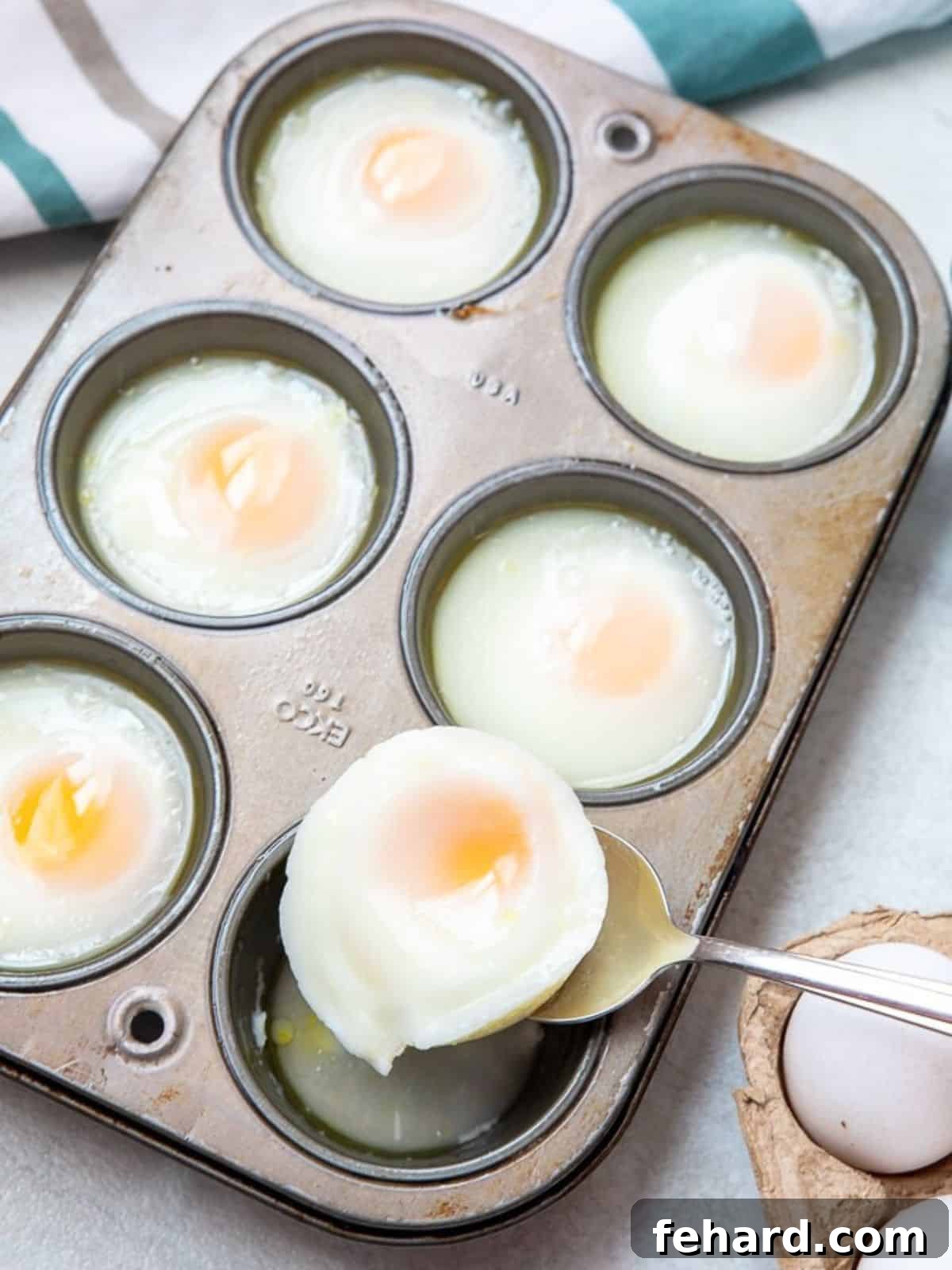 Poached Eggs Removal A spoon gently scooping a perfectly oven-poached egg from a muffin tin, illustrating the careful removal process.