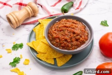 Speedy Blender Salsa 14 Homemade salsa presented in a gray bowl, with tortilla chips and fresh tomatoes nearby.