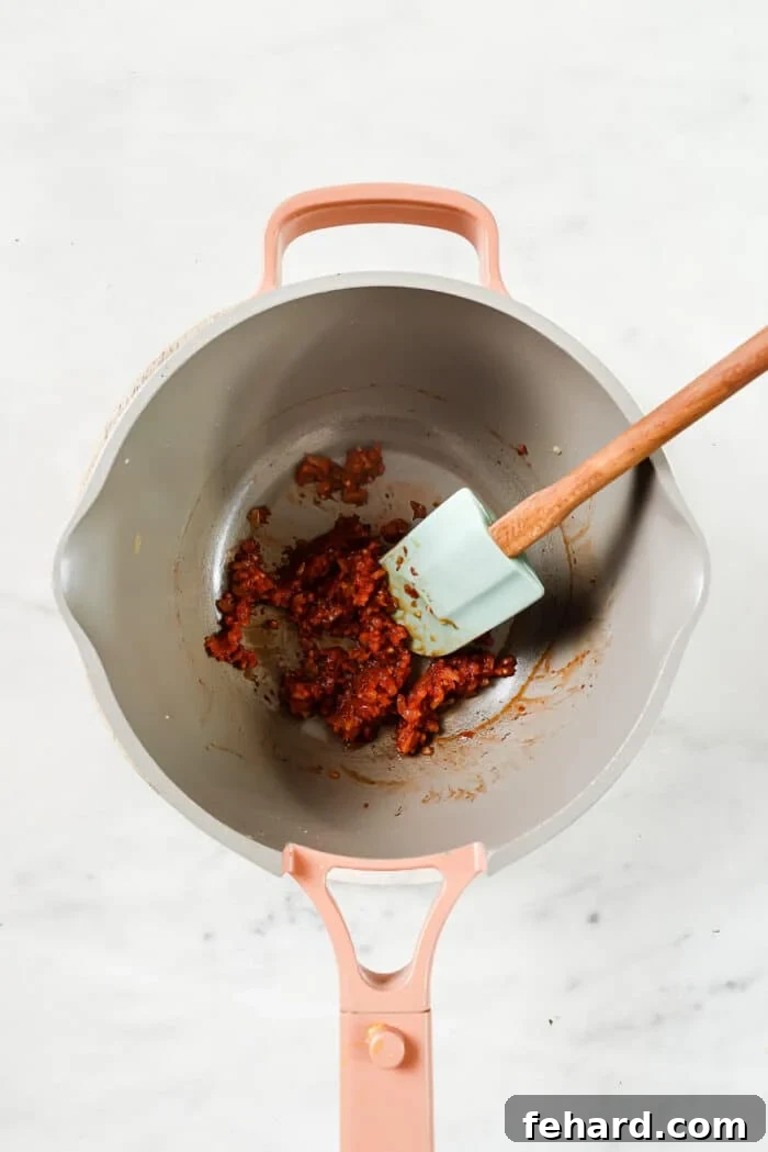 The Secret to Perfect Homemade Tomato Sauce 4 Tomato paste being stirred into the sautéed onions and garlic in a pan, deepening the flavor base for the sauce.