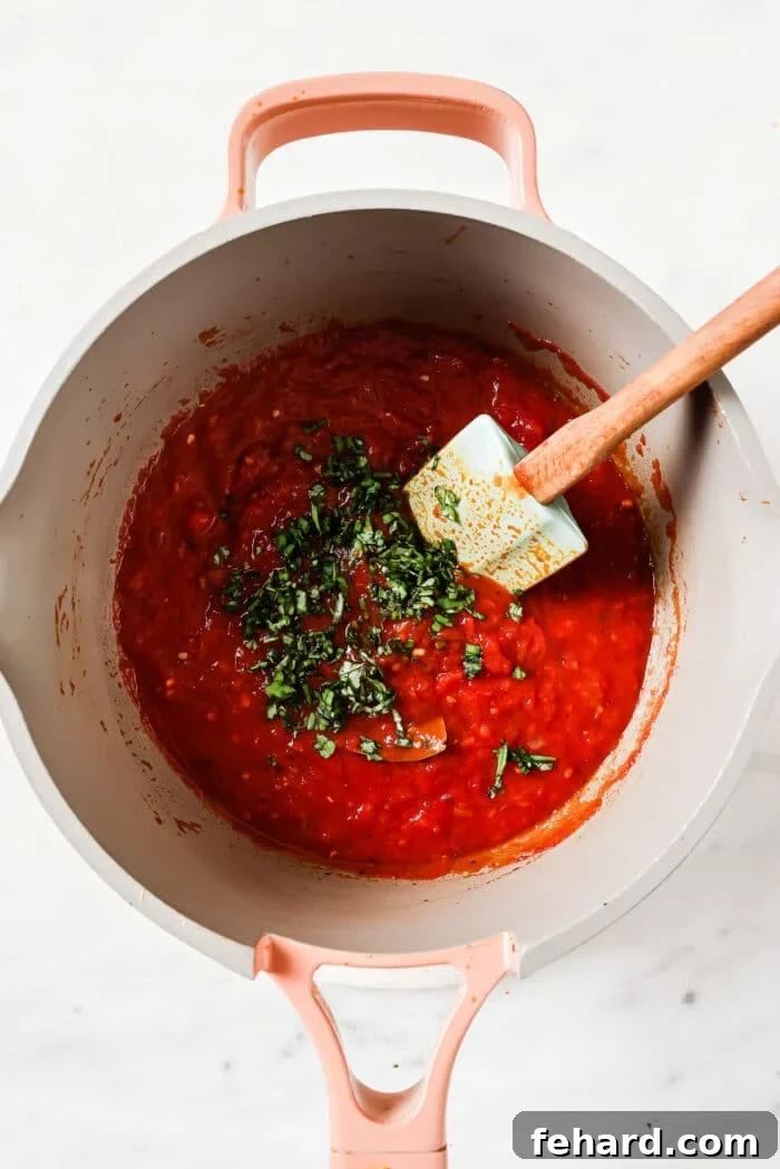 The Secret to Perfect Homemade Tomato Sauce 7 Fresh basil being stirred into the finished tomato sauce after it's removed from heat, adding a final touch of brightness.