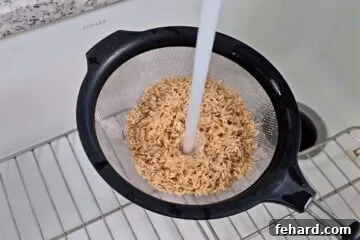 Brown rice inside fine mesh strainer with cold tap water being ran over it.