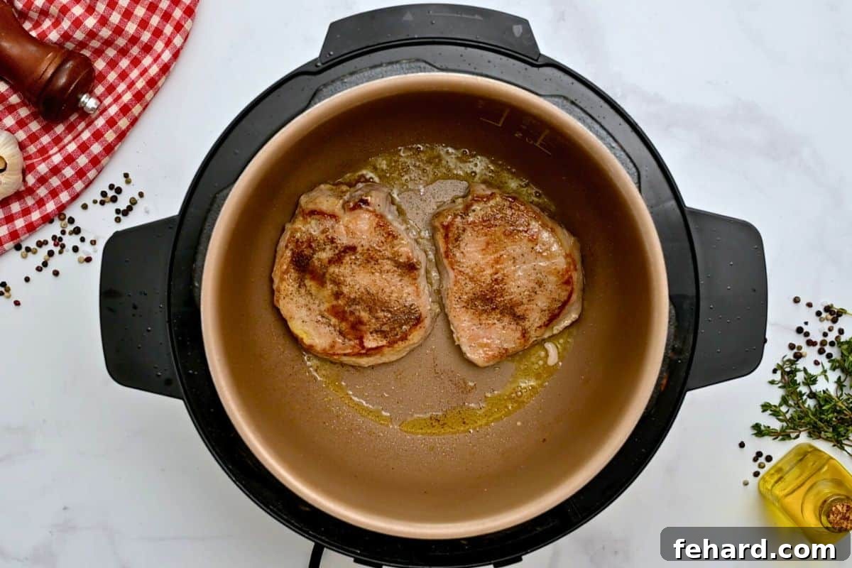 Two seasoned pork chops inside the Instant Pot inner pot after being seared to a golden brown.