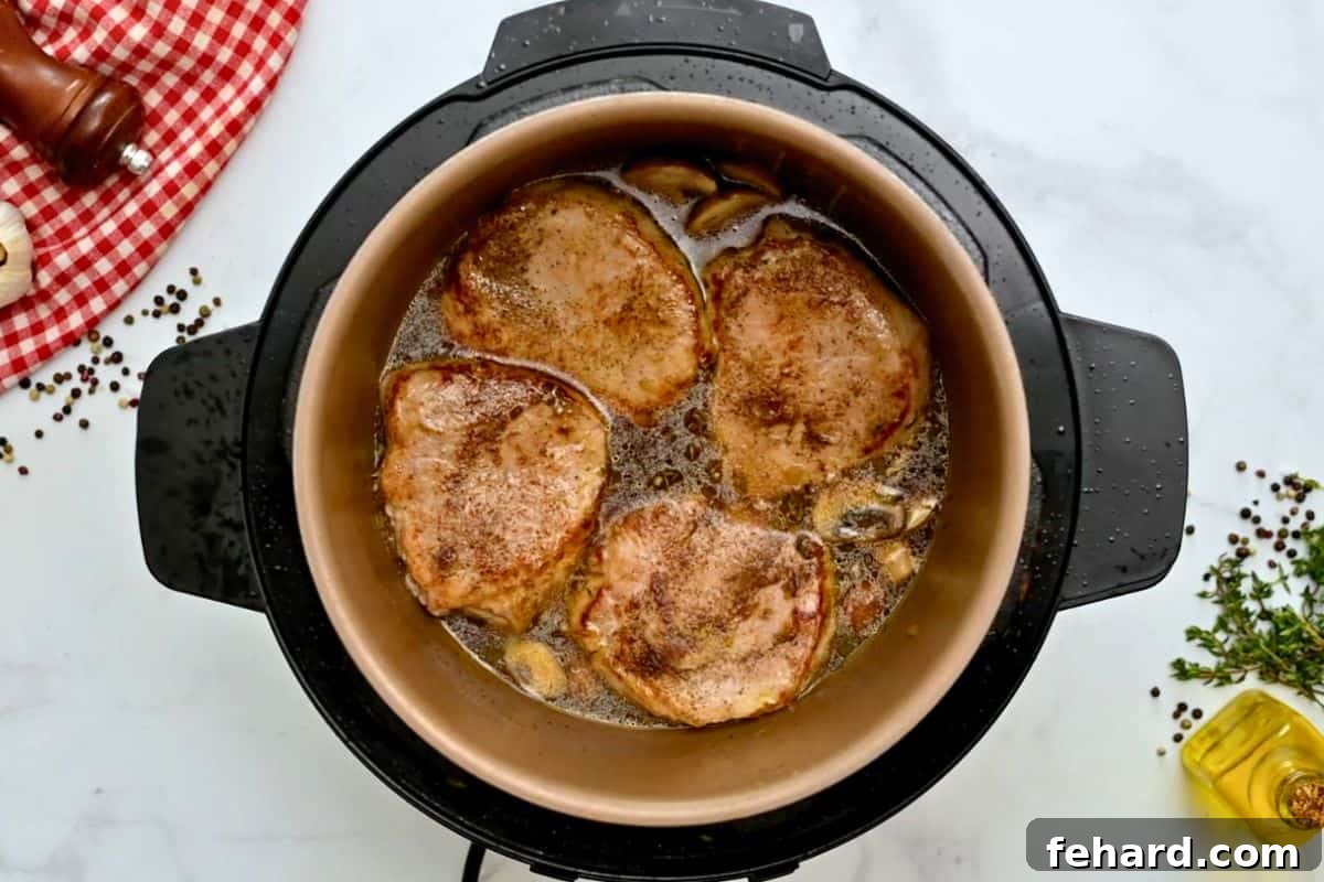 Seared pork chops placed back into the Instant Pot with beef stock and sautéed mushrooms, ready for pressure cooking.
