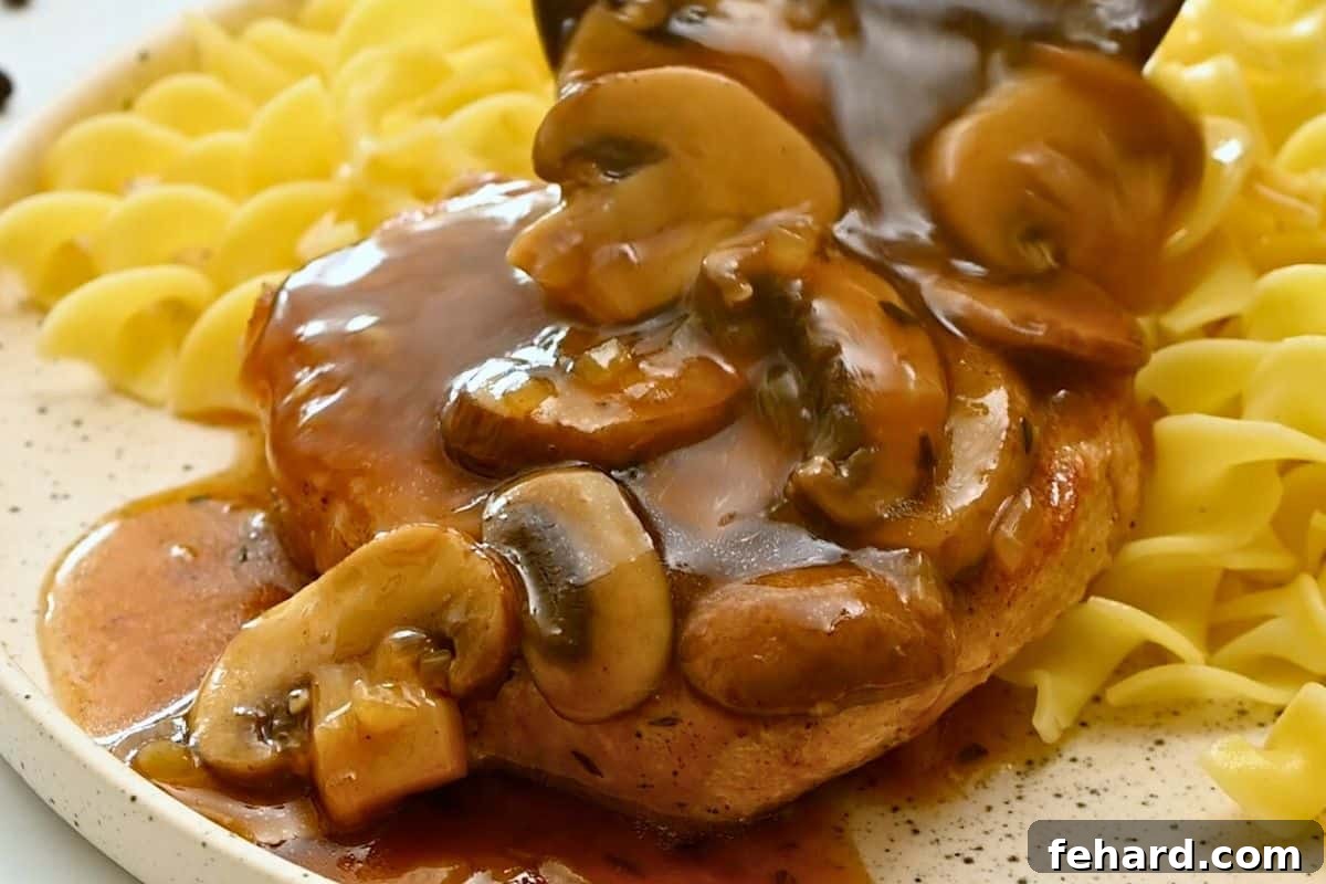 Rich mushroom gravy being poured over a pressure cooked pork chop, served alongside buttered egg noodles.