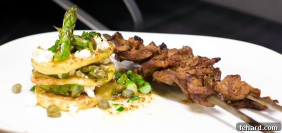 A thoughtfully composed plate featuring savory beef satay alongside perfectly layered potato Napoleons and tender grilled asparagus, creating a balanced and appealing meal.