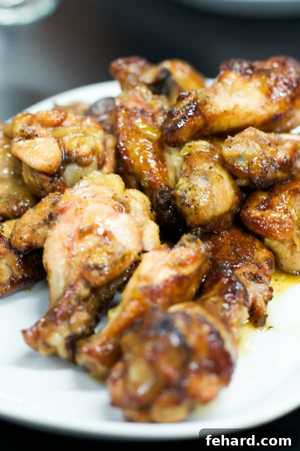 Perfectly smoked chicken drumsticks, glistening with a vibrant orange honey glaze, artfully arranged on a pristine white serving plate.