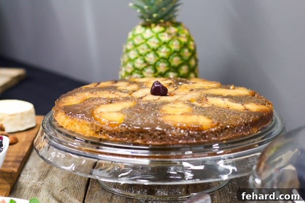 A perfectly golden grilled pineapple upside-down cake, proudly presented on a refined glass cake stand, with a fresh pineapple subtly hinting at its origins in the background.