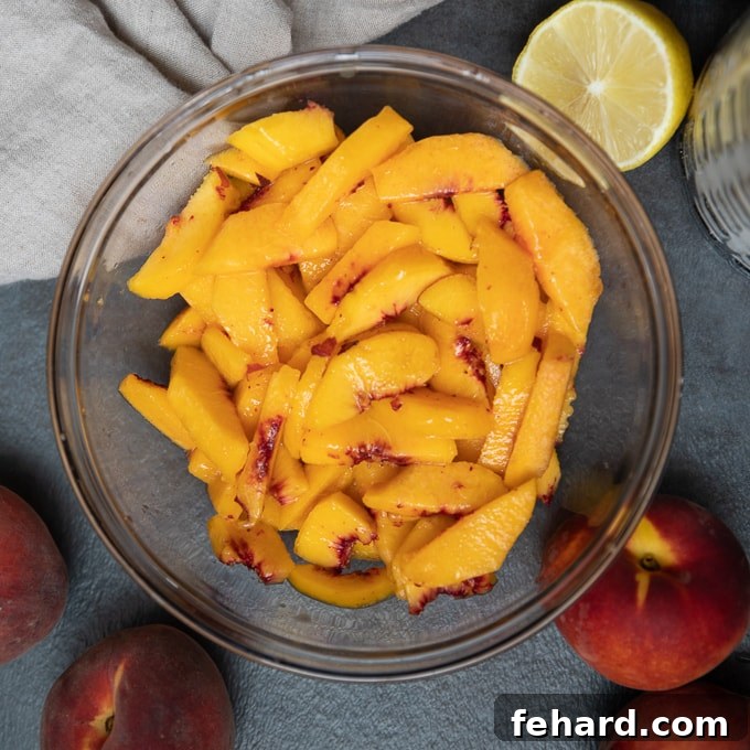 Sliced peaches in a mixing bowl, perfectly tossed with lemon juice, sugar, cinnamon, and nutmeg, forming the base for the crisp filling.