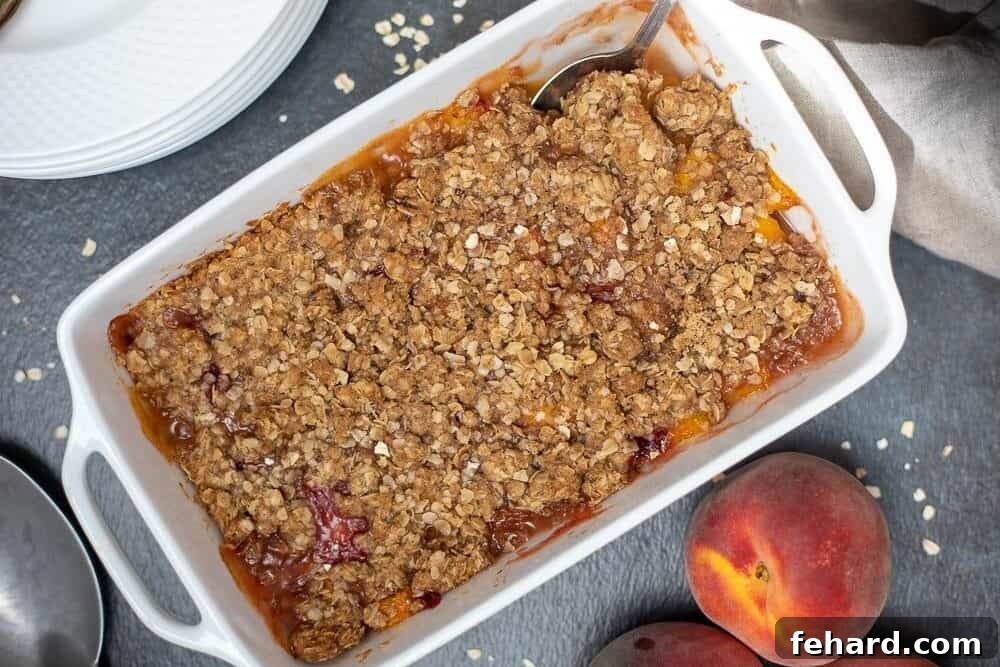 Freshly baked peach crisp in a elegant white ceramic casserole dish, displaying a golden brown, bubbly surface.