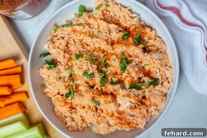 Buffalo Chicken Recipe Shredded buffalo chicken in a white bowl with creamy, spicy sauce, accompanied by carrots and celery