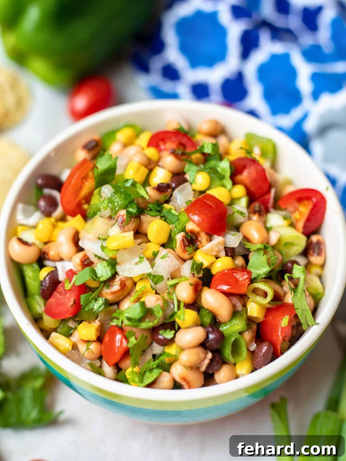 Texas Caviar - The Best Cowboy Caviar Recipe A colorful bowl of Texas Caviar, featuring black-eyed peas, black beans, corn, and diced tomatoes, garnished with fresh cilantro and green onions, served next to a pile of crispy tortilla chips.
