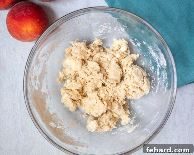 Biscuit Cobbler Topping in clear mixing bowl next to fresh peaches. 