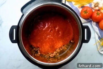 Spaghetti noodles topped with sauteed beef and tomato sauce layered inside inner pot.