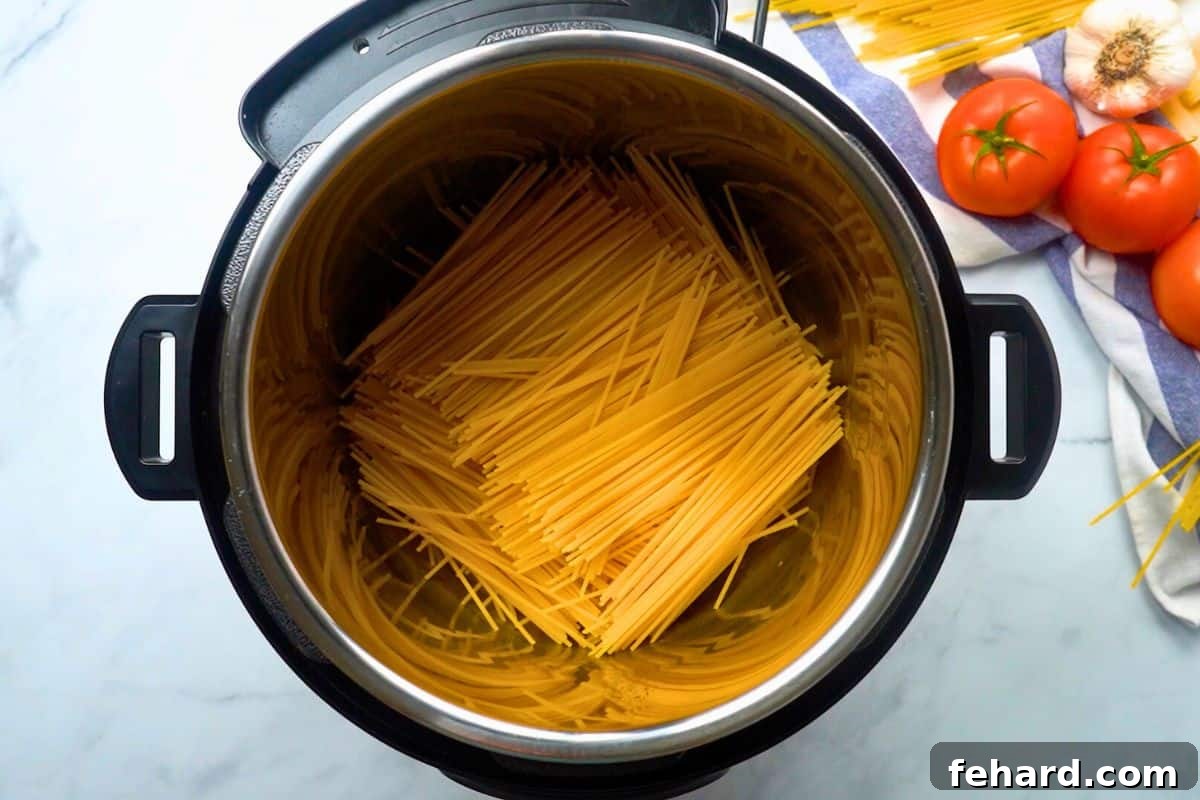 Broken spaghetti noodles carefully layered in a crisscrossing pattern inside the Instant Pot's inner pot, ready for the next ingredients.