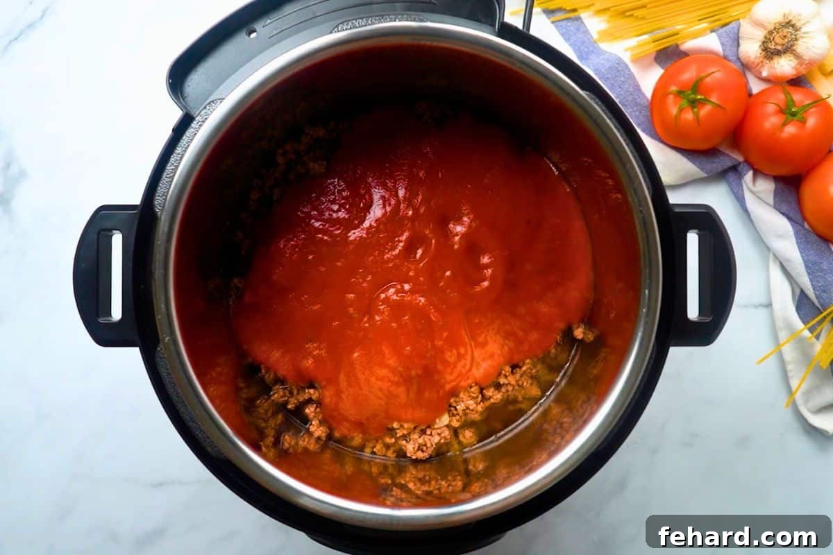 Spaghetti noodles topped with sautéed ground beef and a rich tomato sauce, layered precisely inside the Instant Pot before cooking.