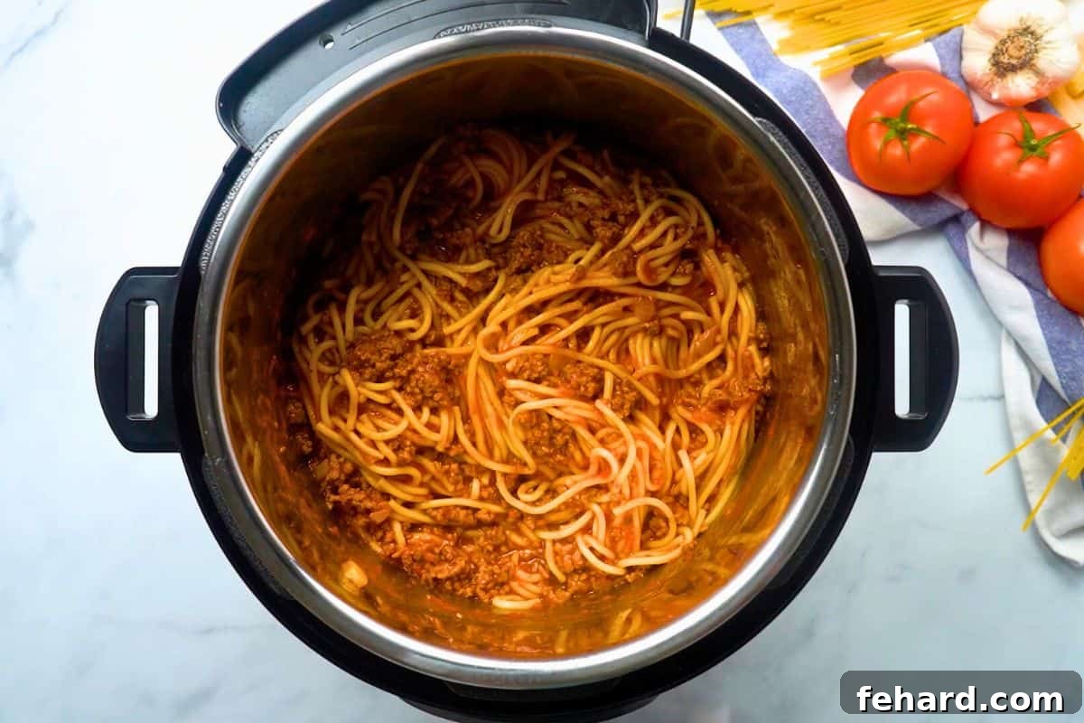 Perfectly cooked, tender spaghetti noodles thoroughly mixed with a rich meat sauce inside the Instant Pot's inner pot, ready to be served.