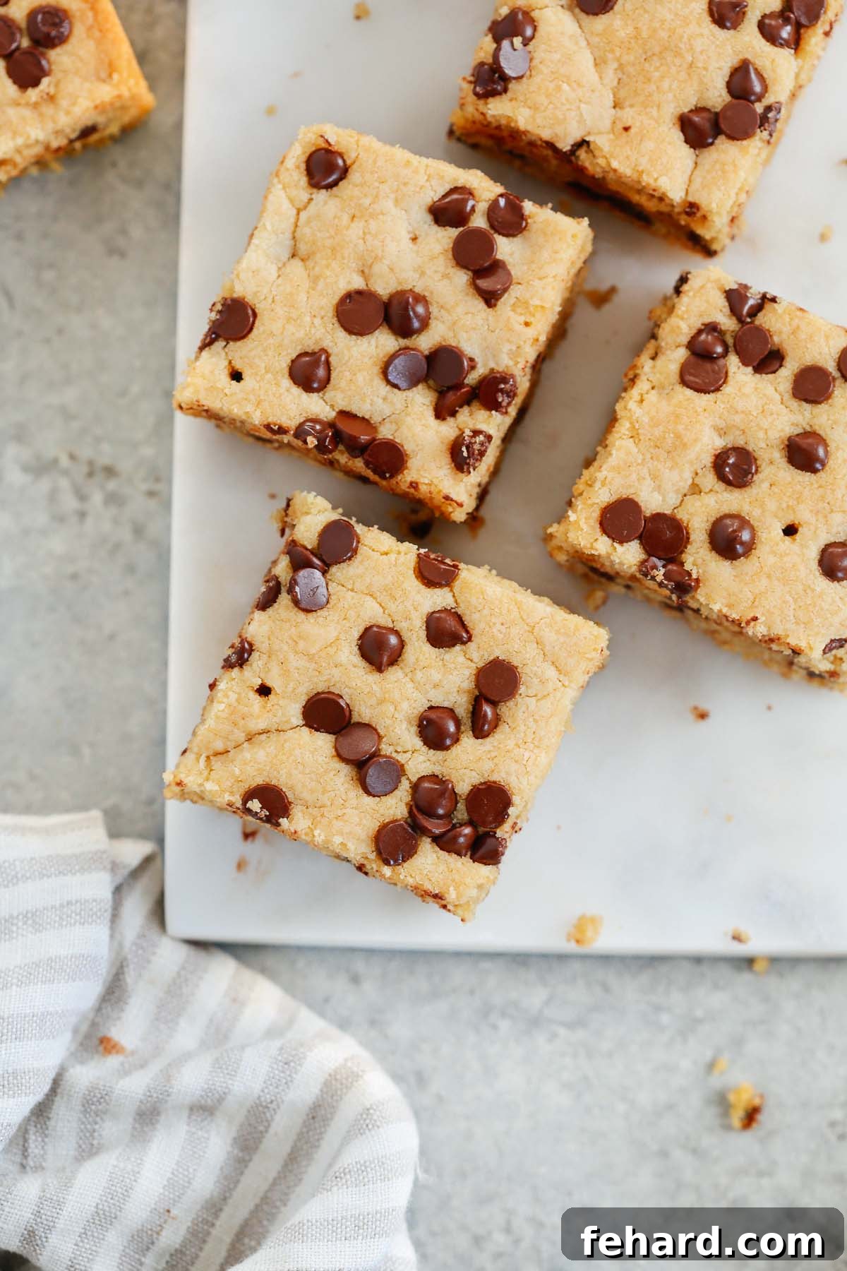 Overhead photo of four perfectly cut squares of healthier chocolate chip cookie bars, showing their golden-brown edges and soft centers.