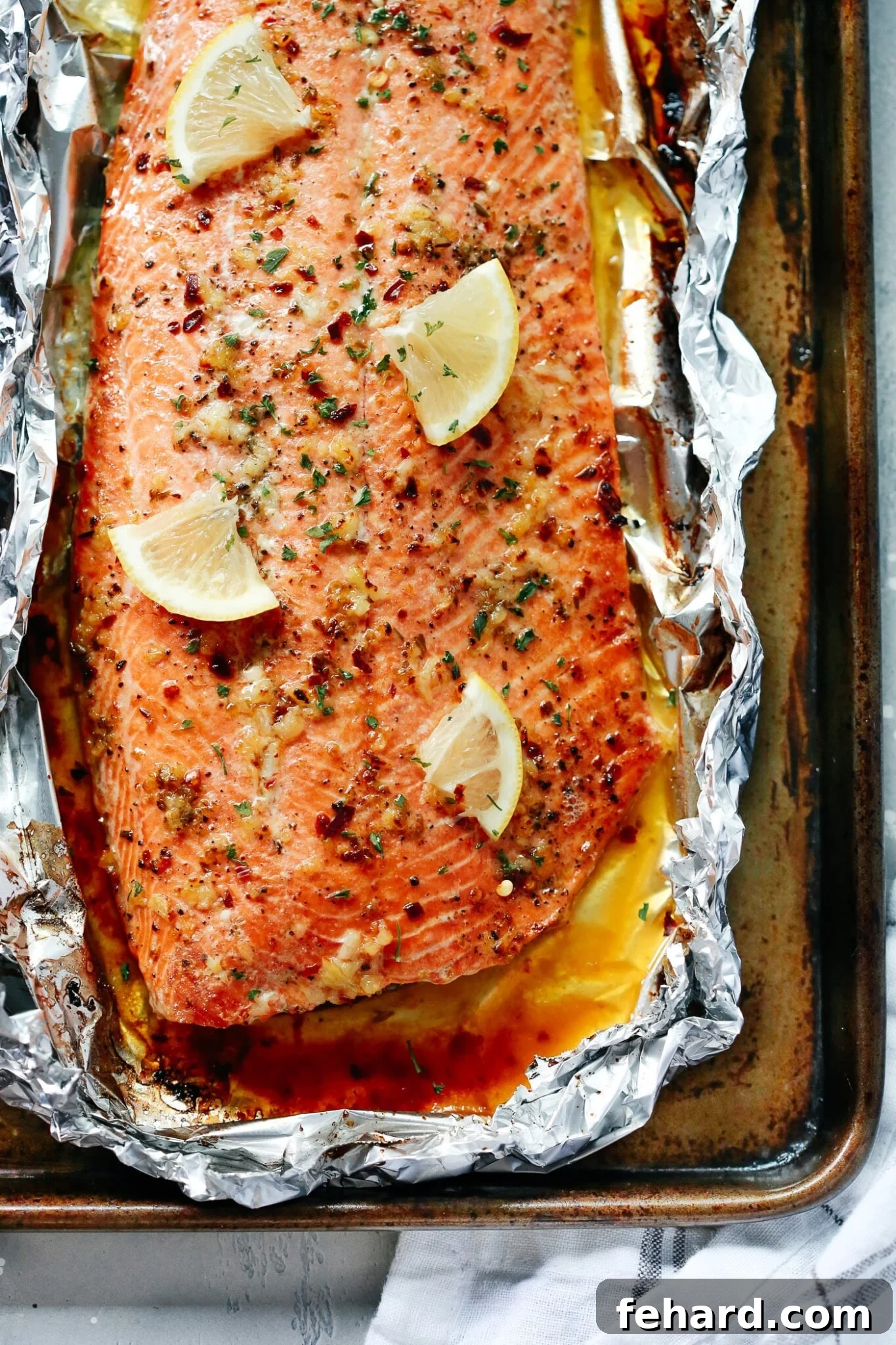 Closeup view of perfectly baked salmon in foil with vibrant lemon slices and a rich garlic butter sauce.