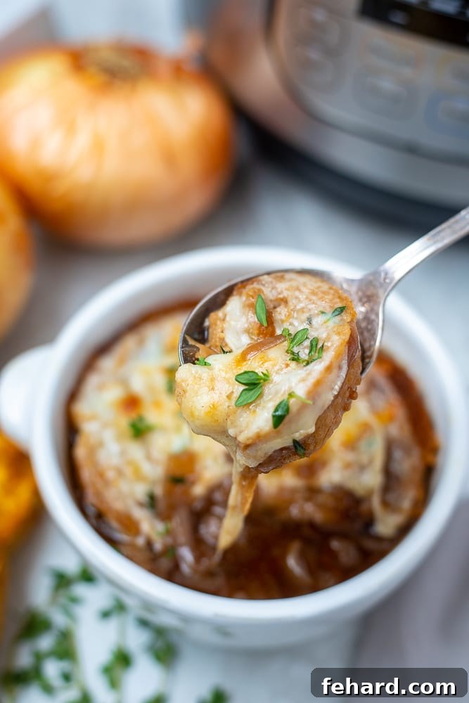 A steaming bowl of Instant Pot French Onion Soup, topped with a cheesy bread crouton, with a spoon gently lifting to show a delicious cheese pull.
