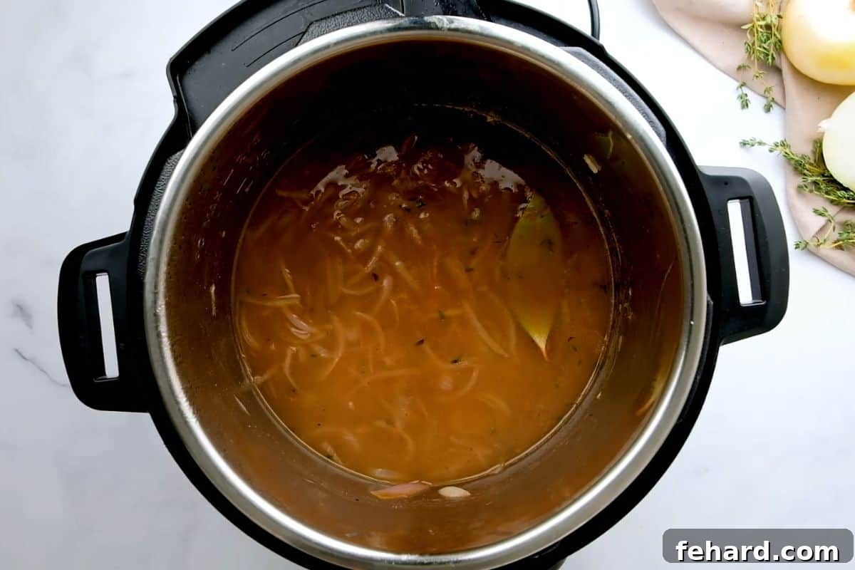 All the essential ingredients – onions, rich beef broth, bay leaves, and seasonings – layered perfectly in the Instant Pot inner pot, ready for pressure cooking.