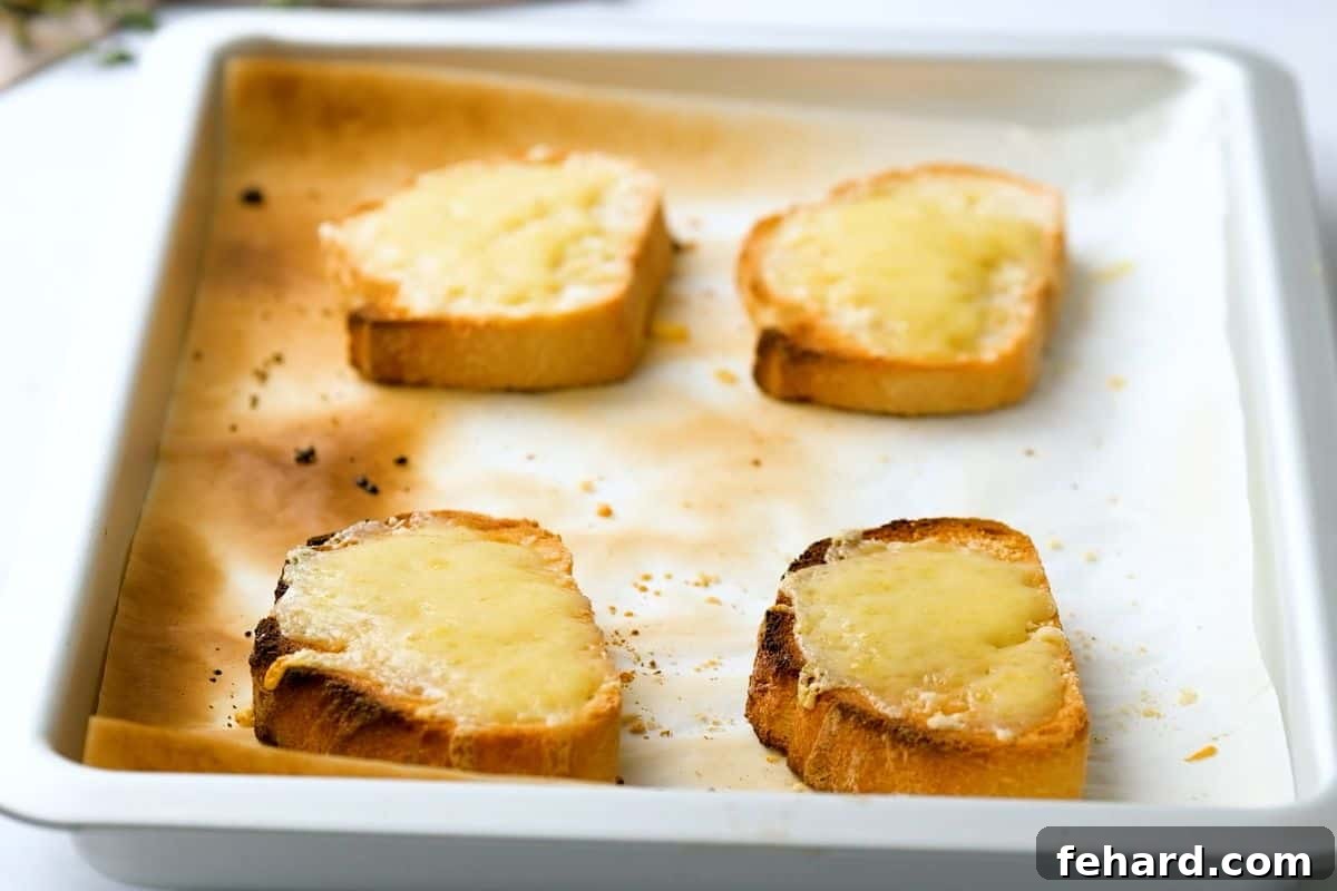 Golden toasted French bread slices on a sheet pan, generously topped with melted Swiss and Parmesan cheese, ready to crown your French Onion Soup.