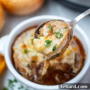 Spoonful of Instant Pot French Onion Soup with cheese pulling out of soup bowl.