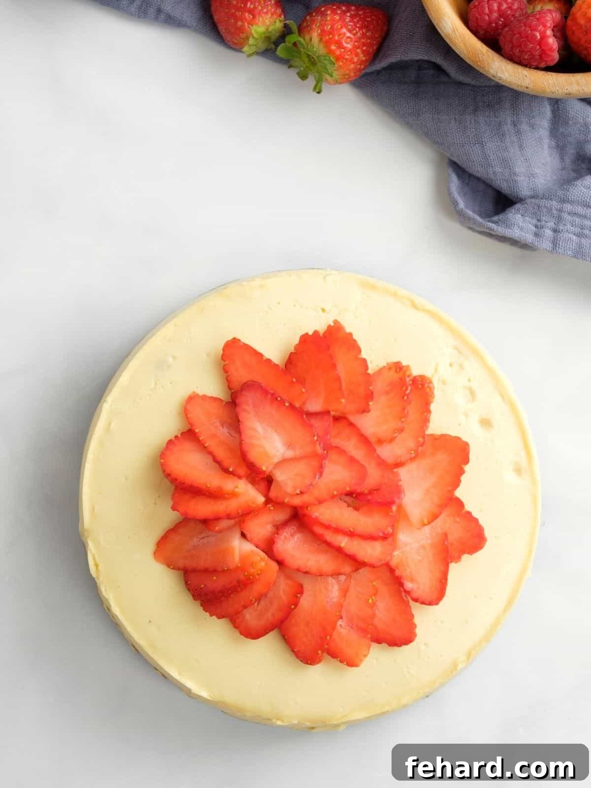 Instant Pot Cheesecake topped with glistening sliced strawberries, with a scattering of fresh berries in the background, ready to be enjoyed.