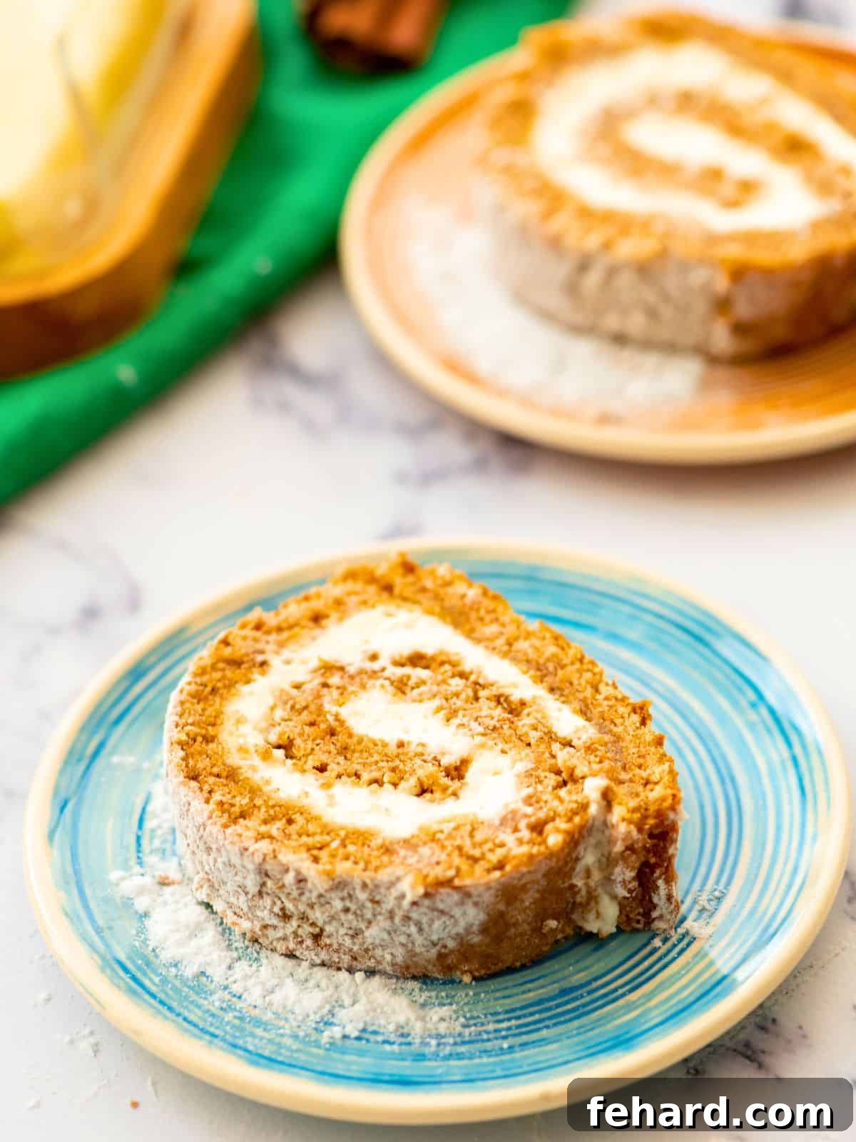 Pumpkin Roll Recipe - Easy Fall Dessert A slice of homemade pumpkin roll cake with airy pumpkin sponge cake and thick and creamy cream cheese filling on plate dusted with powdered sugar, ready to be enjoyed.