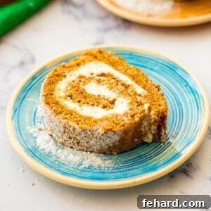 Slice of homemade pumpkin roll showing light pumpkin cake with cream cheese swirl, perfect for fall holidays.