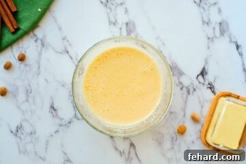 Whipped eggs, sugar, lemon juice, and pumpkin puree mixed together in a large bowl, forming the wet batter base.