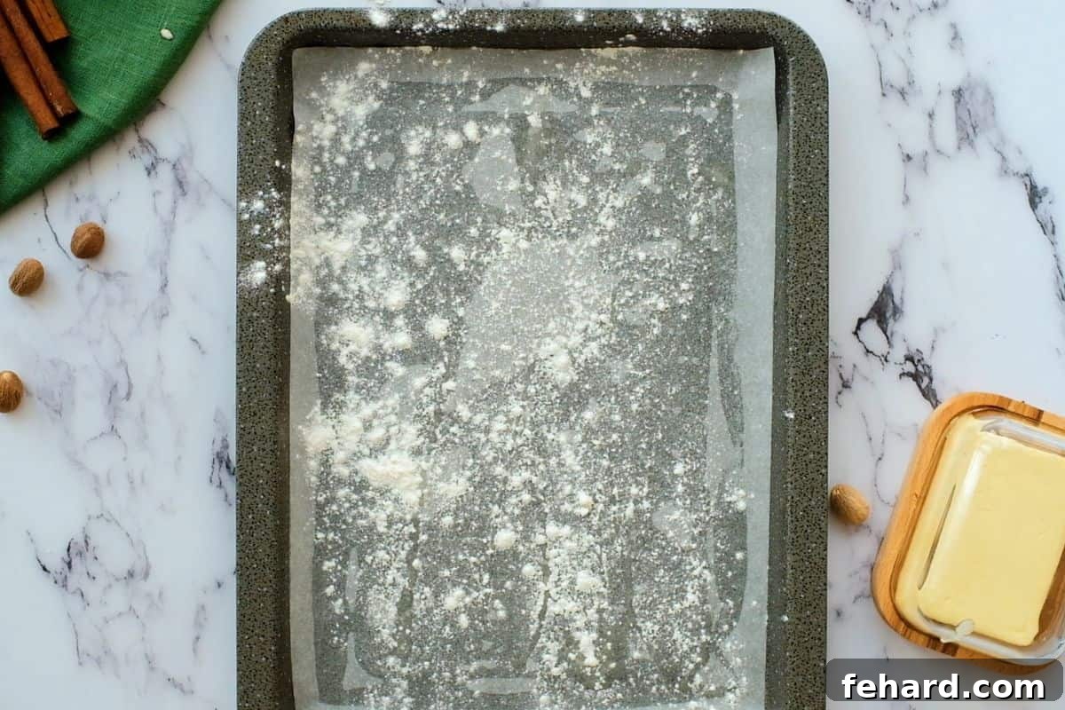 Recipe for Pumpkin Roll Cake Pan Prep A jelly roll sheet pan meticulously lined with parchment paper, greased, and lightly dusted with flour, ready for pumpkin cake batter.