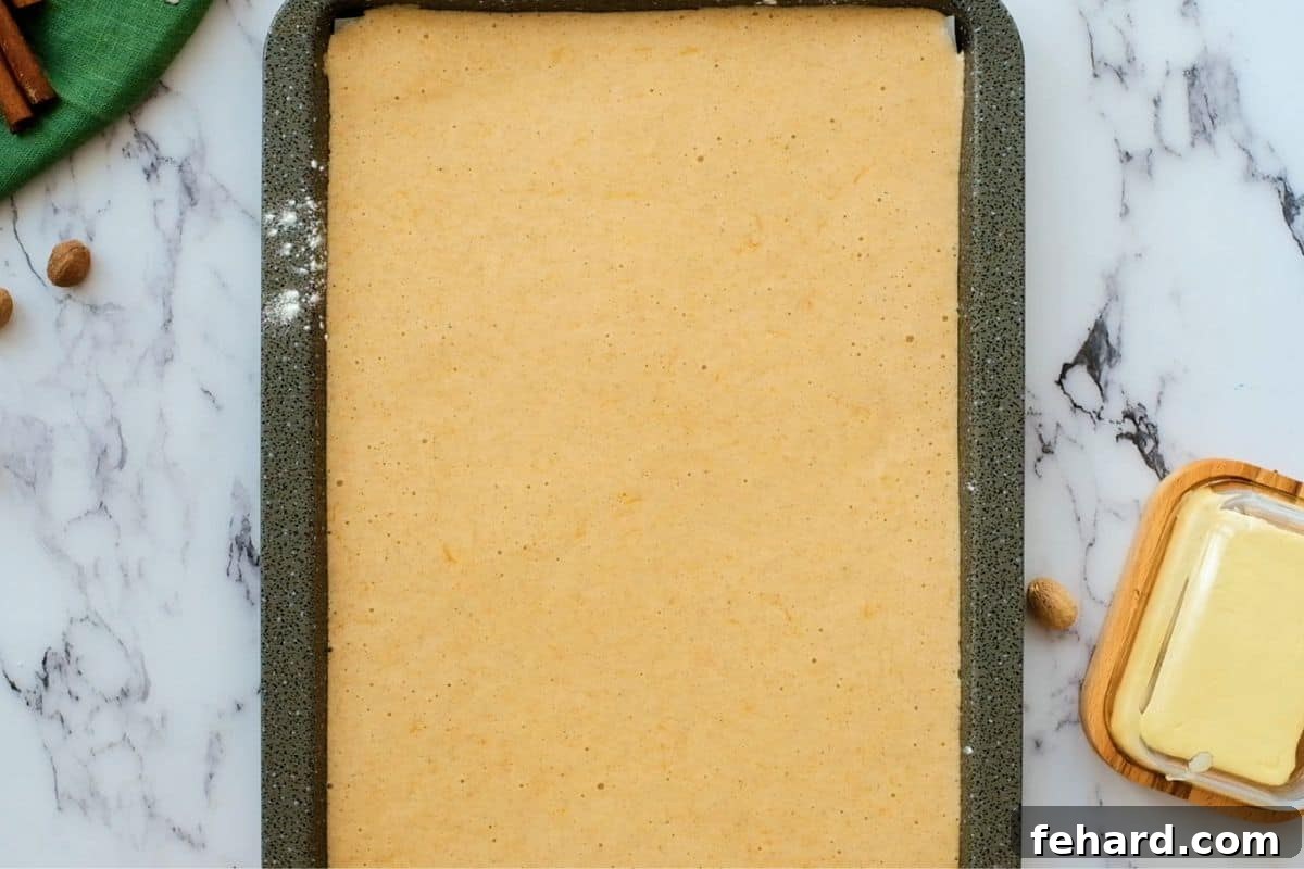Pumpkin Roll Recipe Batter in Pan Smooth pumpkin roll batter evenly spread across a prepared sheet pan, ready to be baked into a thin, pliable cake.