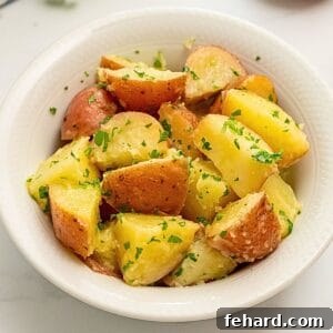 A small serving dish filled with perfectly buttered red potatoes, generously garnished with fresh parsley.