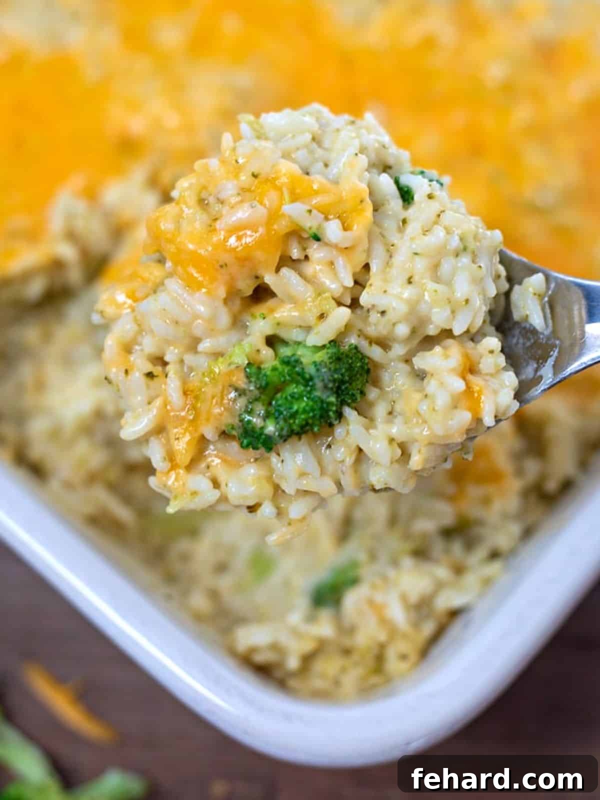 A serving of homemade cheesy broccoli rice casserole being scooped from a baking dish, showcasing its creamy texture and golden top.