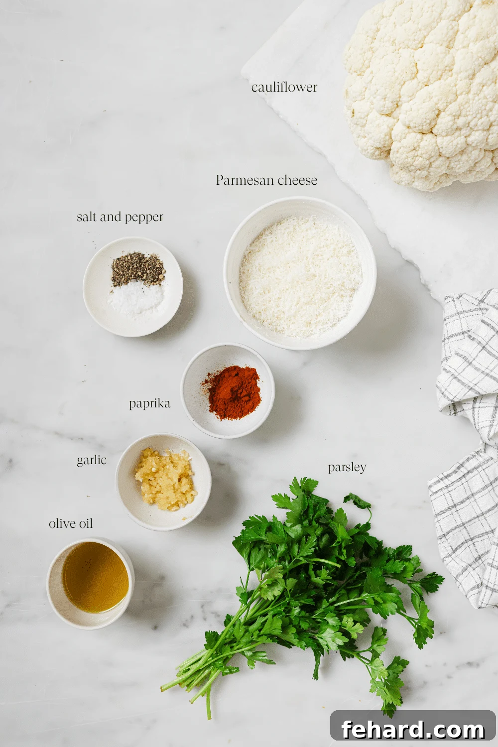 Pre-measured ingredients for roasted cauliflower, including a head of cauliflower, olive oil, garlic, parmesan, and spices.