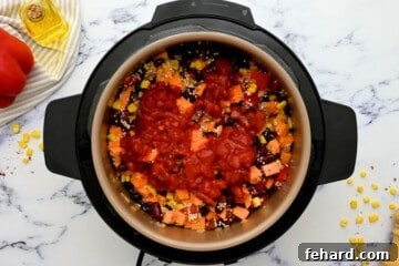 Ingredients for sweet potato black bean chili layered in instant pot with diced tomatoes on top of chili mixture.
