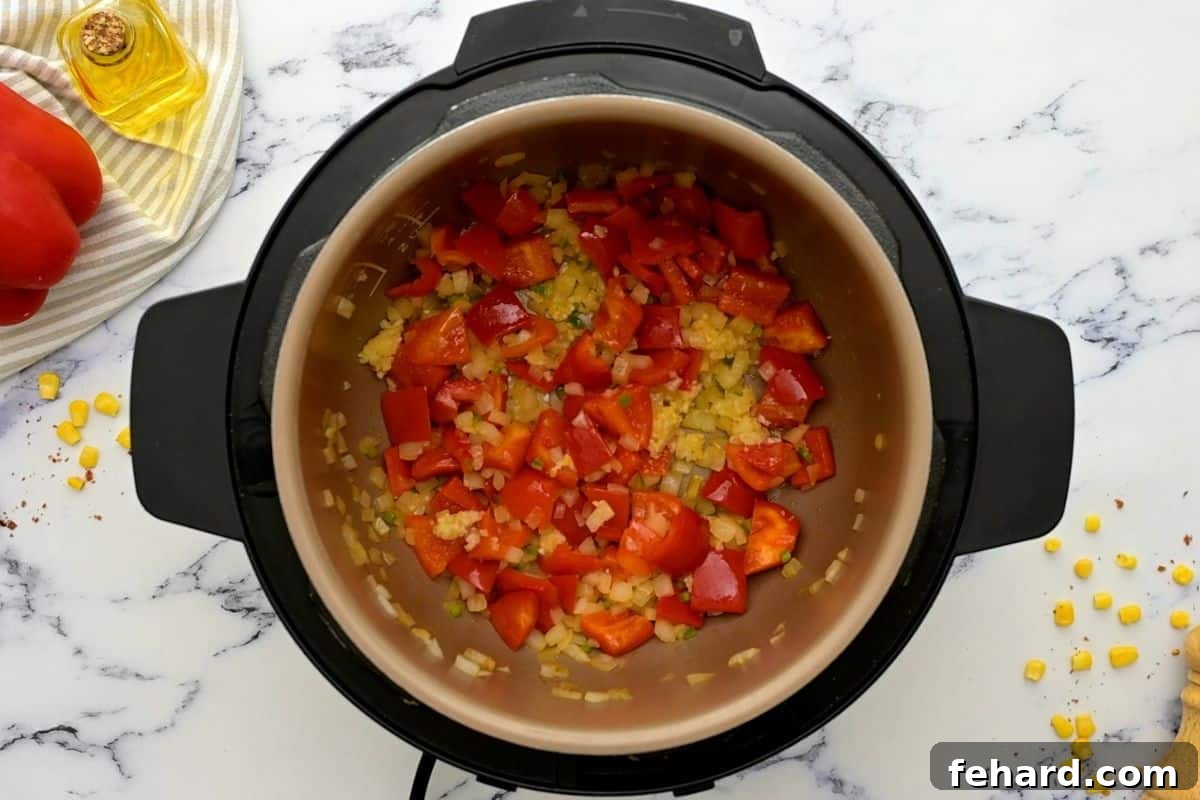 Freshly chopped onions, red bell peppers, and jalapeños sizzling in olive oil inside the Instant Pot's inner pot during the sautéing process, creating an aromatic base for the chili.
