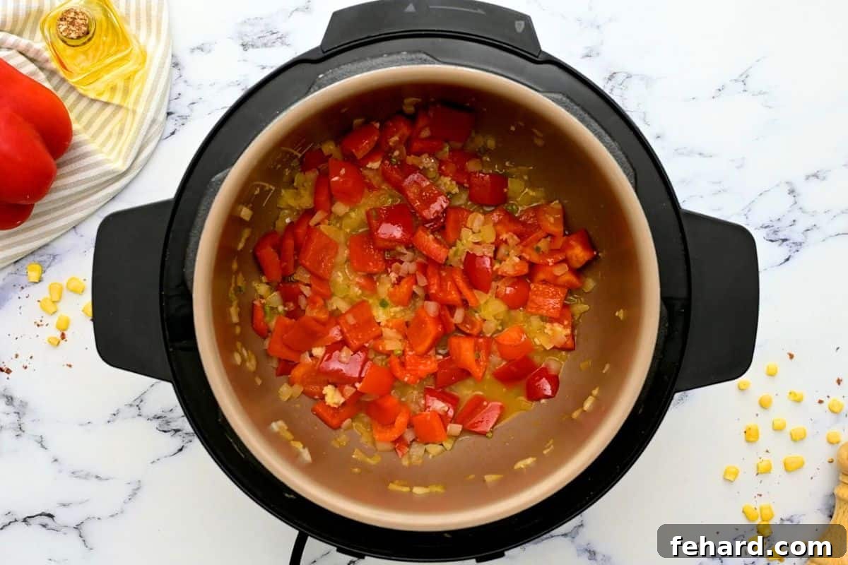 Close-up of the Instant Pot's inner pot, showing sauteed red bell pepper and onions alongside a small amount of broth being used to deglaze the bottom, ensuring no bits are stuck.