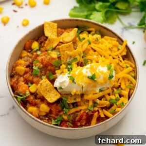 Bowl of sweet potato quinoa chili topped with sour cream and corn chips.