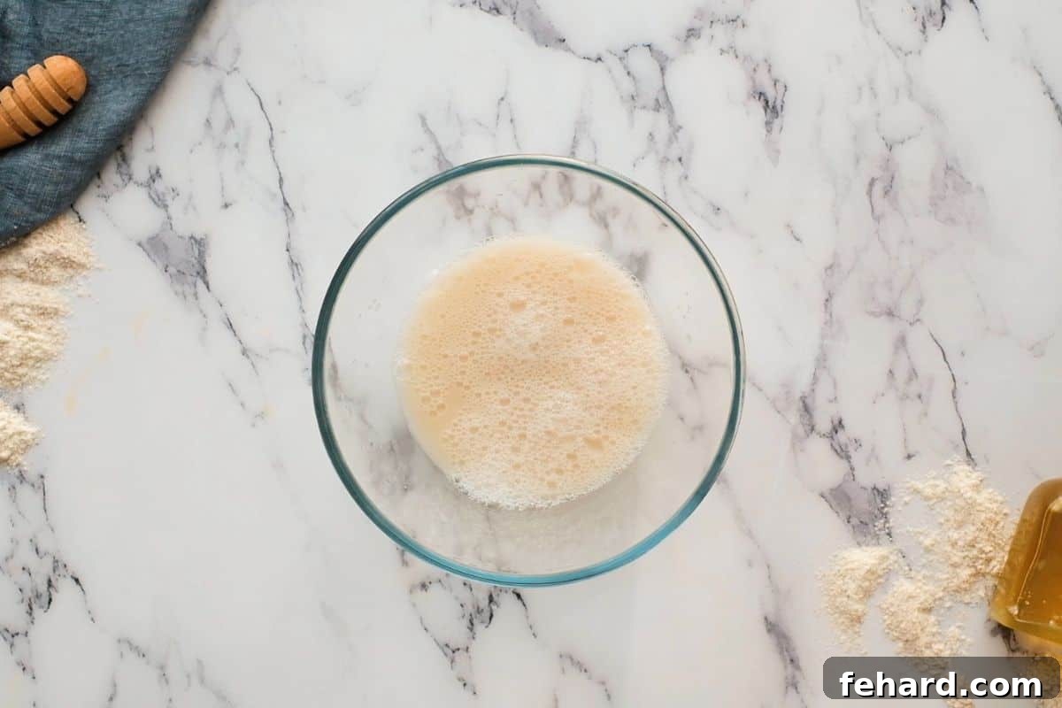 Yeast foaming in mixing bowl with whole wheat flour in background, indicating activity.
