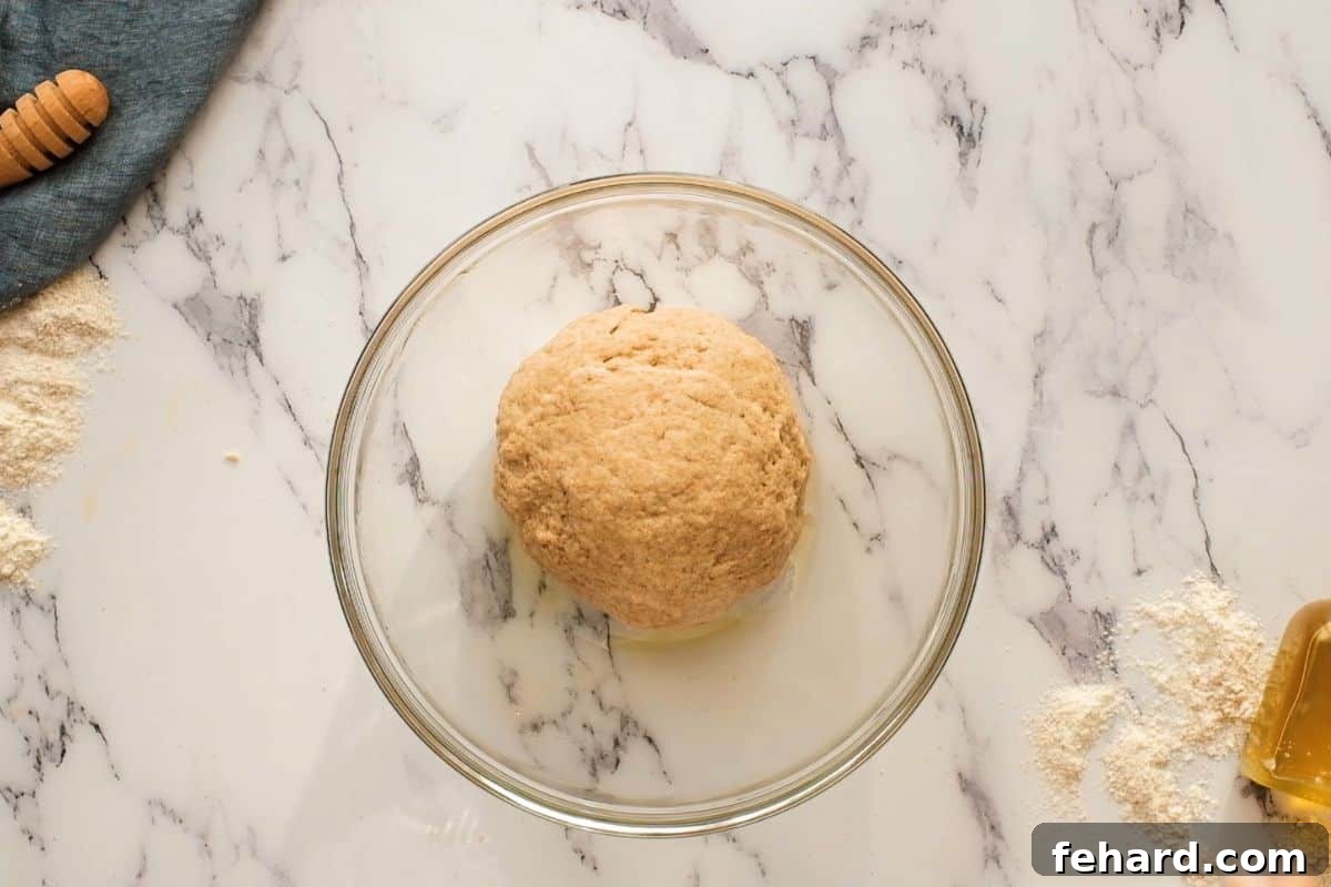 Smooth, elastic wheat dough for rolls resting in a glass bowl.