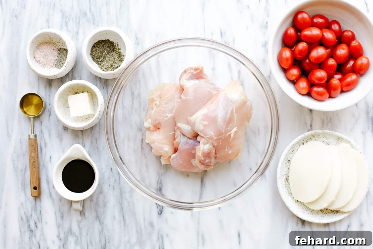 A flat lay of fresh ingredients laid out on a white surface, including chicken thighs, tomatoes, mozzarella, and herbs, ready to be prepared for baked caprese chicken.