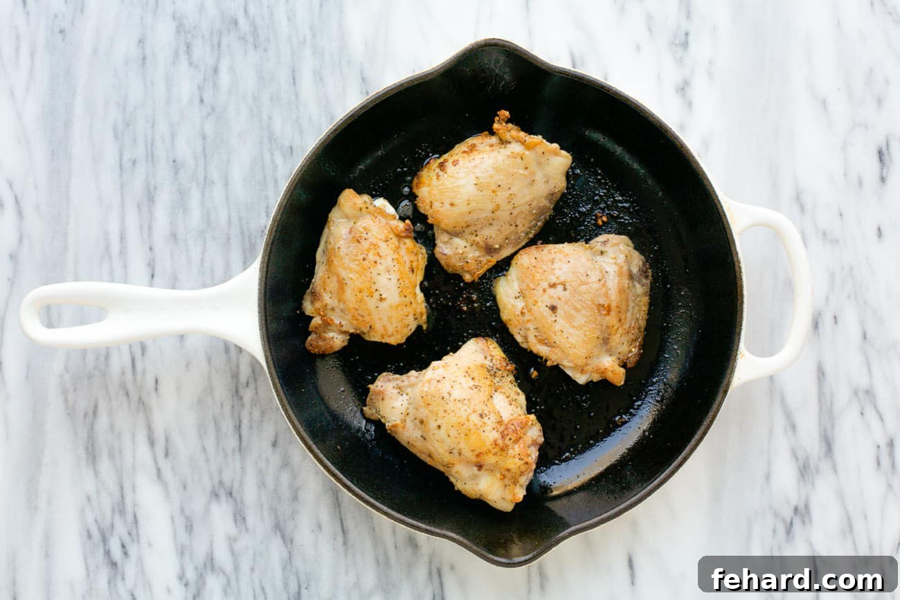 Crispy seared chicken thighs sizzling in a cast iron skillet, golden brown and ready for the oven.