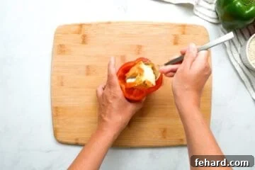 Spoon scooping out ribs and seeds from cavity of bell pepper.