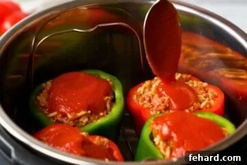 Spoon pouring topping tomato sauce on 4 stuffed peppers inside instant pot on trivet.