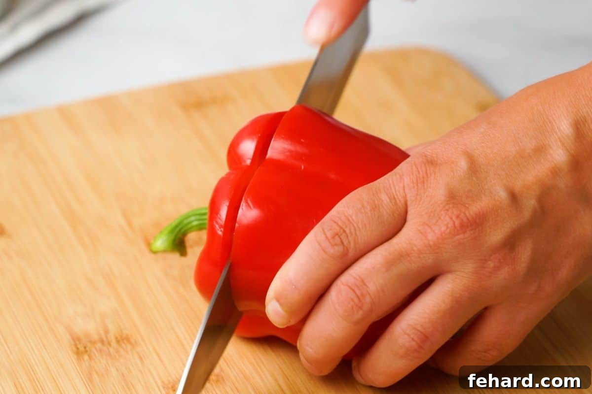Cutting Bell Pepper Tops A sharp knife carefully slicing off the top of a red bell pepper, preparing it for stuffing.