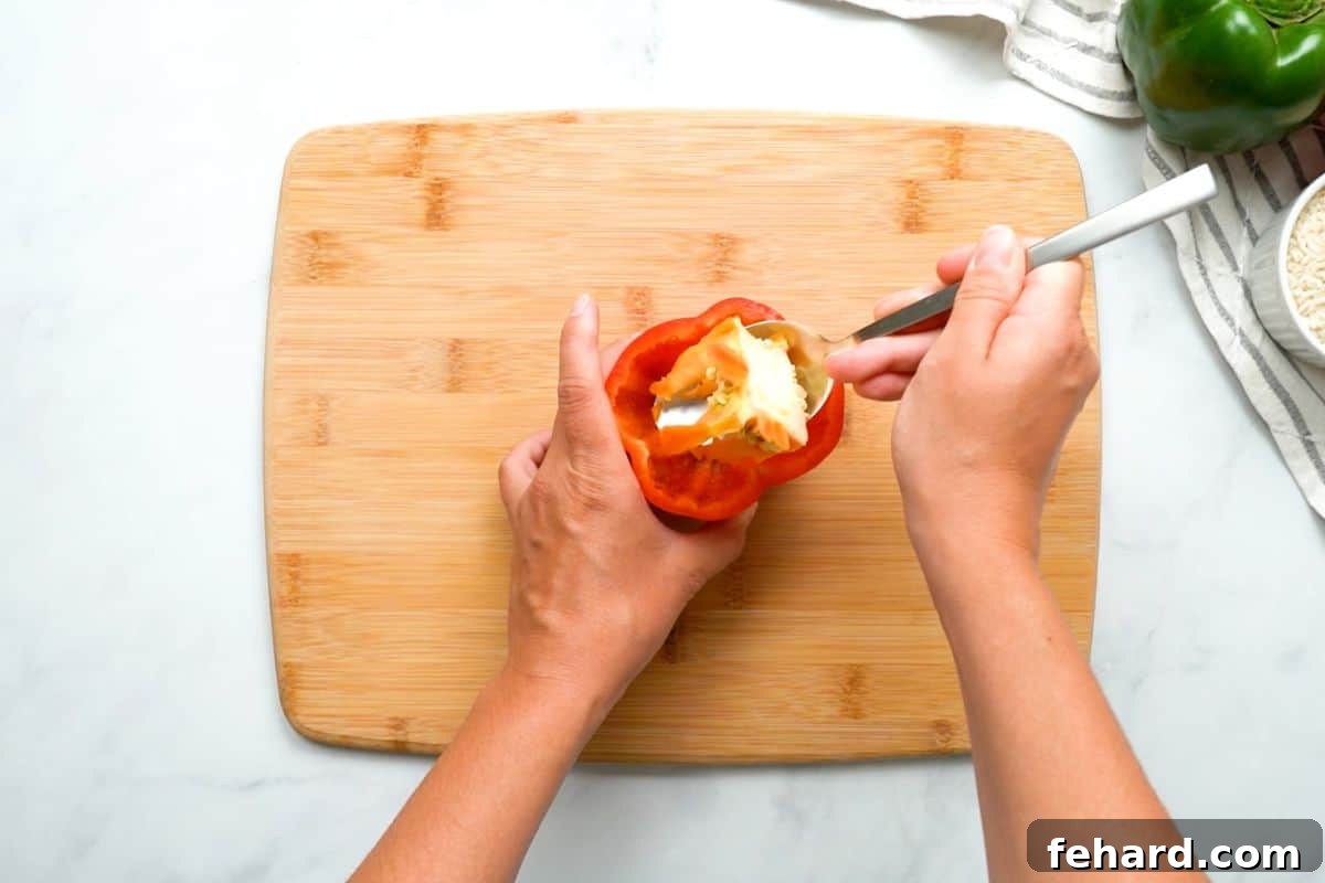 Cleaning Pepper Cavity A spoon efficiently scooping out the seeds and white ribs from the hollowed-out cavity of a bell pepper.